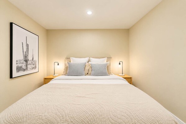 A bedroom with a large bed, two bedside lamps, and a framed picture on the wall.