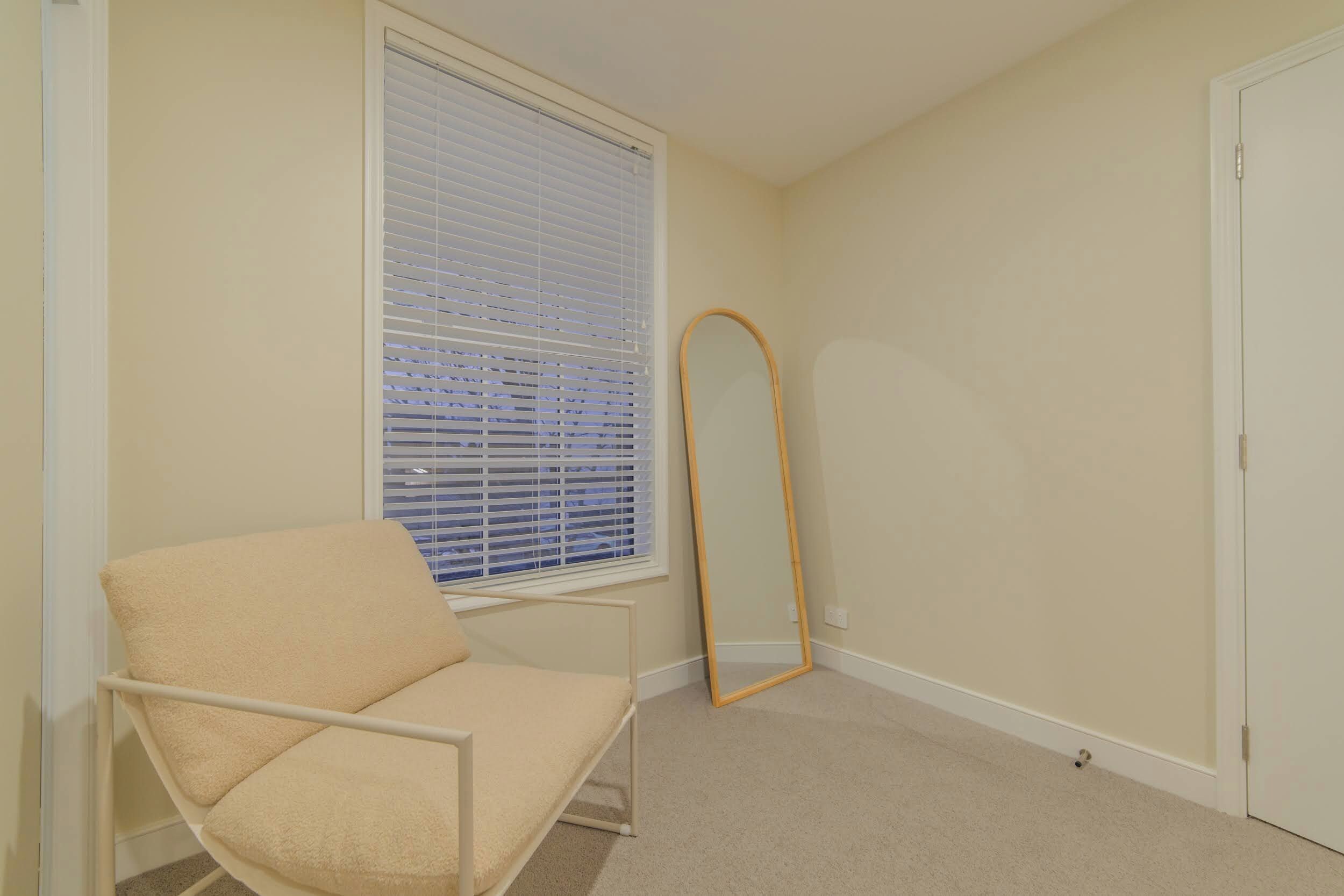 A bedroom with a single bed, a window with blinds, a standing mirror, and a door.