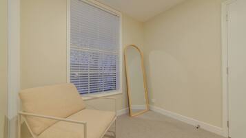 A bedroom with a single bed, a window with blinds, a standing mirror, and a door.