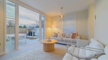 Un salon moderne avec un canapé blanc, une table basse ronde et une grande fenêtre équipée de stores.