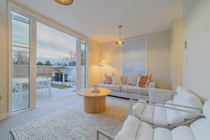 A modern living room with a white sofa, a round coffee table, and a large window with blinds.