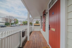 A wooden porch with a red door, white railings, and a mailbox.