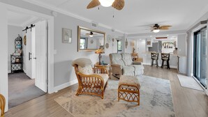 A spacious living room with a ceiling fan, a large mirror, and a dining area with a kitchen in the background. - 2B/2B Fairview Isles 121 Condo, Walk to Beach, Heated Pool! (Fort Myers Beach)