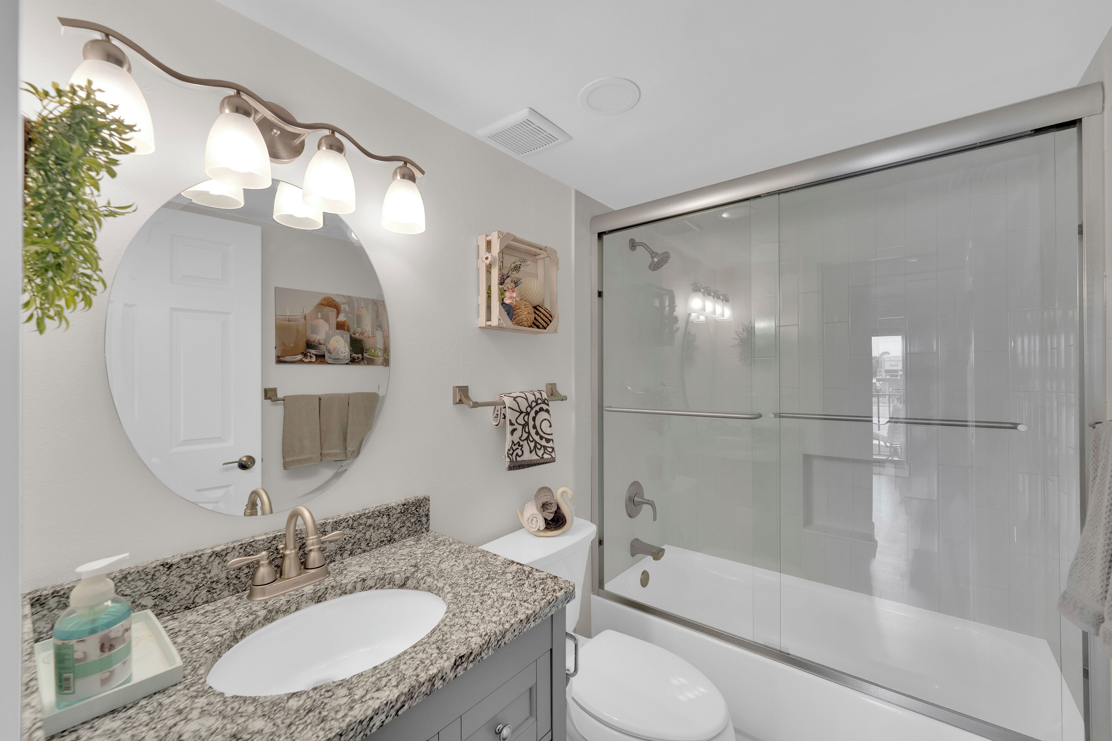 A bathroom with a granite countertop sink, a large mirror, a glass shower enclosure, and a toilet.