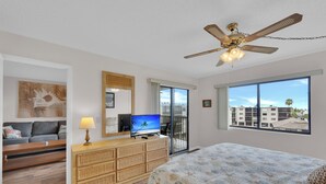 Et hotelværelse med seng, fjernsyn, loftventilator, balkon med udsigt og spiseplads med bord og stole.