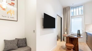 Un salon moderne avec un canapé, un téléviseur à écran plat fixé au mur et un coin repas comprenant une table en bois et des tabourets.