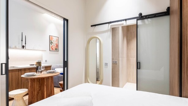 Une chambre d’hôtel moderne avec un lit, une table ronde en bois recouverte d’une nappe blanche, un miroir et un placard à portes coulissantes.