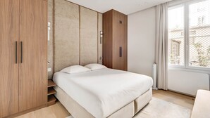 A bedroom with a bed, wooden wardrobe, and a window with curtains. - Suite Prestige in Pigalle (Paris)