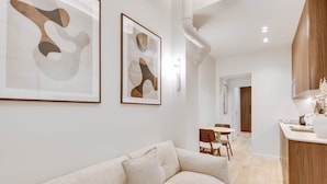 A modern living room with a beige sofa, a dining area with a wooden table and chairs, and a kitchen with wooden cabinets. - Suite Prestige in Pigalle (Paris)