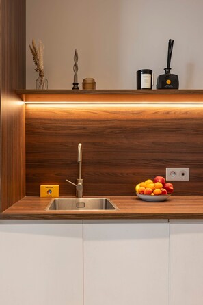 A modern kitchen with a stainless steel sink, wooden countertop, and a bowl of fruit.