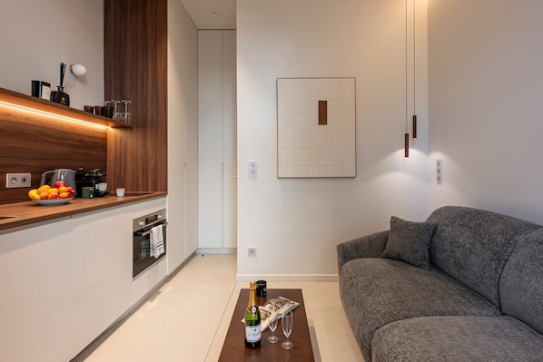 A modern kitchen with a wooden countertop, a built-in oven, and a dining area with a grey sofa.