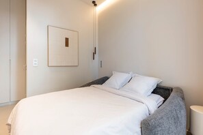 A neatly made bed with white bedding, a gray upholstered headboard, and a wall-mounted light fixture. - Luxury design studio in Paris (Paris)