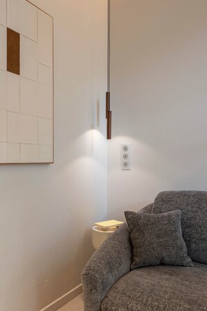 A modern room with a grey sofa, a hanging light fixture, and a wall-mounted power outlet. - Luxury design studio in Paris (Paris)