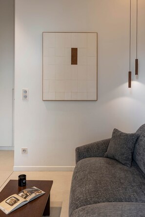 Een moderne woonkamer met een grijze bank, een lijstwerk abstract kunstwerk, een bijzettafeltje met een tijdschrift, en een hanglamp.