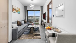Ein modernes Wohnzimmer mit einer grauen Couch, einem Couchtisch und einem Essbereich mit einer Obstplatte und Gläsern.