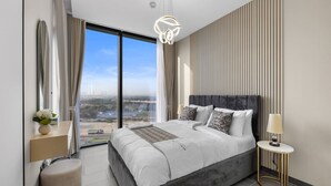 A modern bedroom with a large bed, a view of the city, and a stylish pendant light. - Stylish 1BR Retreat in Sobha Crest w/ Balcony (Dubai)