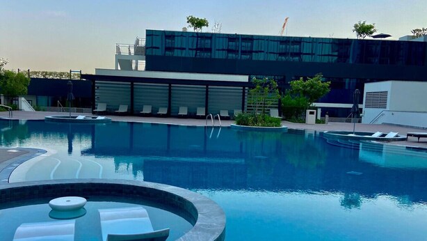 A swimming pool with lounge chairs and a hot tub, surrounded by modern buildings and greenery. - Stylish 1BR Retreat in Sobha Crest w/ Balcony (Dubai)