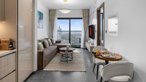 A modern kitchen with a built-in oven, a dining area with a round table and chairs, a sofa, and a balcony with a view. - Stylish 1BR Retreat in Sobha Crest w/ Balcony (Dubai)