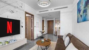 A modern living room with a flat-screen TV, a brown sofa, a wooden coffee table, and a dining area with a white chair. - Stylish 1BR Retreat in Sobha Crest w/ Balcony (Dubai)