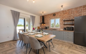 A modern kitchen with a brick wall, a dining area with a wooden table and chairs, and a large refrigerator. - Holiday Home Olivarum with pool (Bila Vlaka)
