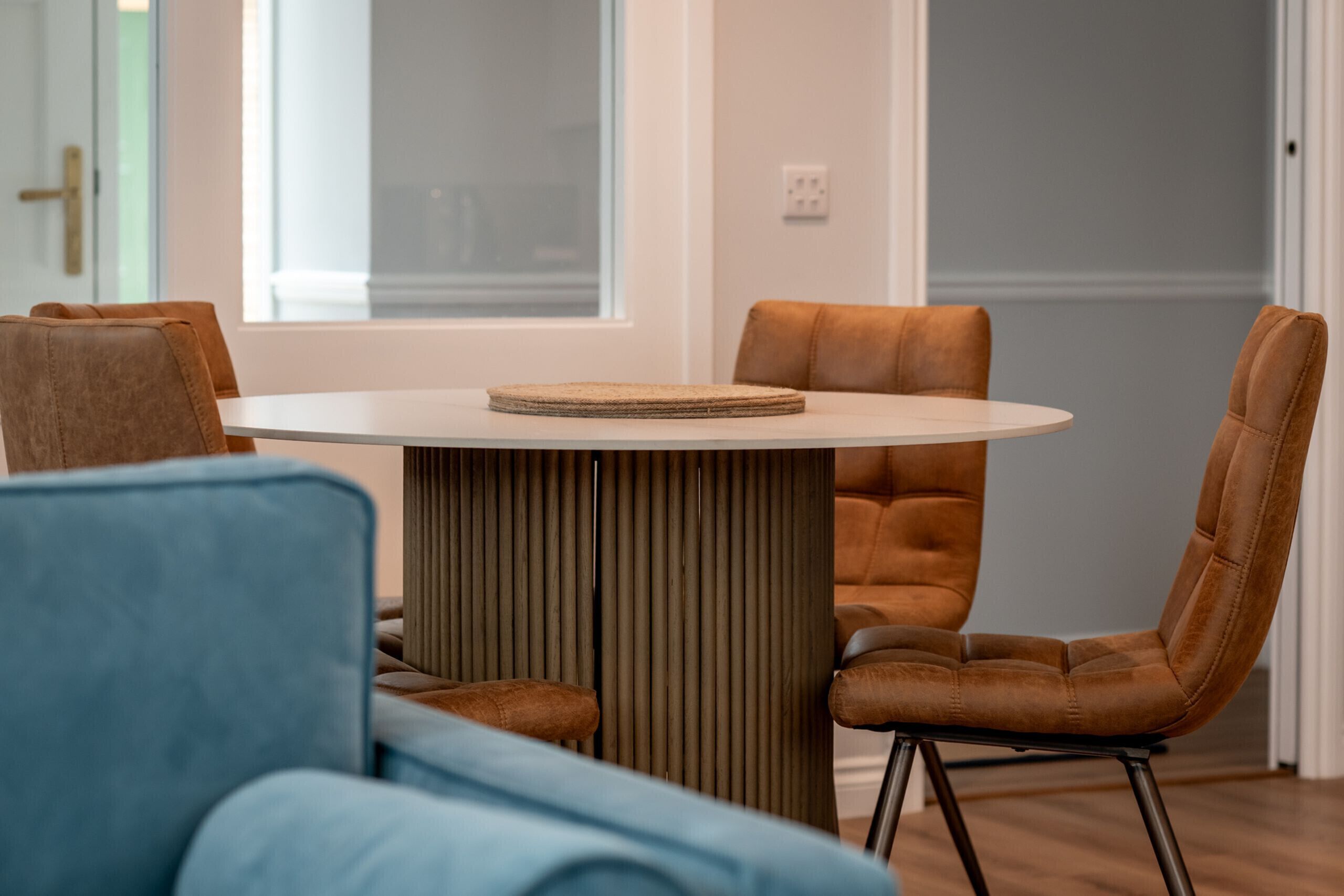 A modern dining area with a round table and four brown leather chairs.