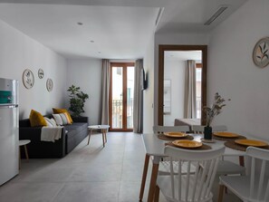Un salon moderne comprenant un canapé, une table à manger avec des chaises, une petite table d’appoint et une plante en pot.