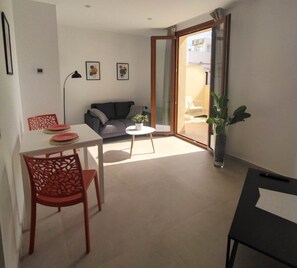 Una sala de estar moderna con un sofá, una mesa de comedor con sillas, una mesita de centro y un ventanal corredero que da a un espacio al aire libre.