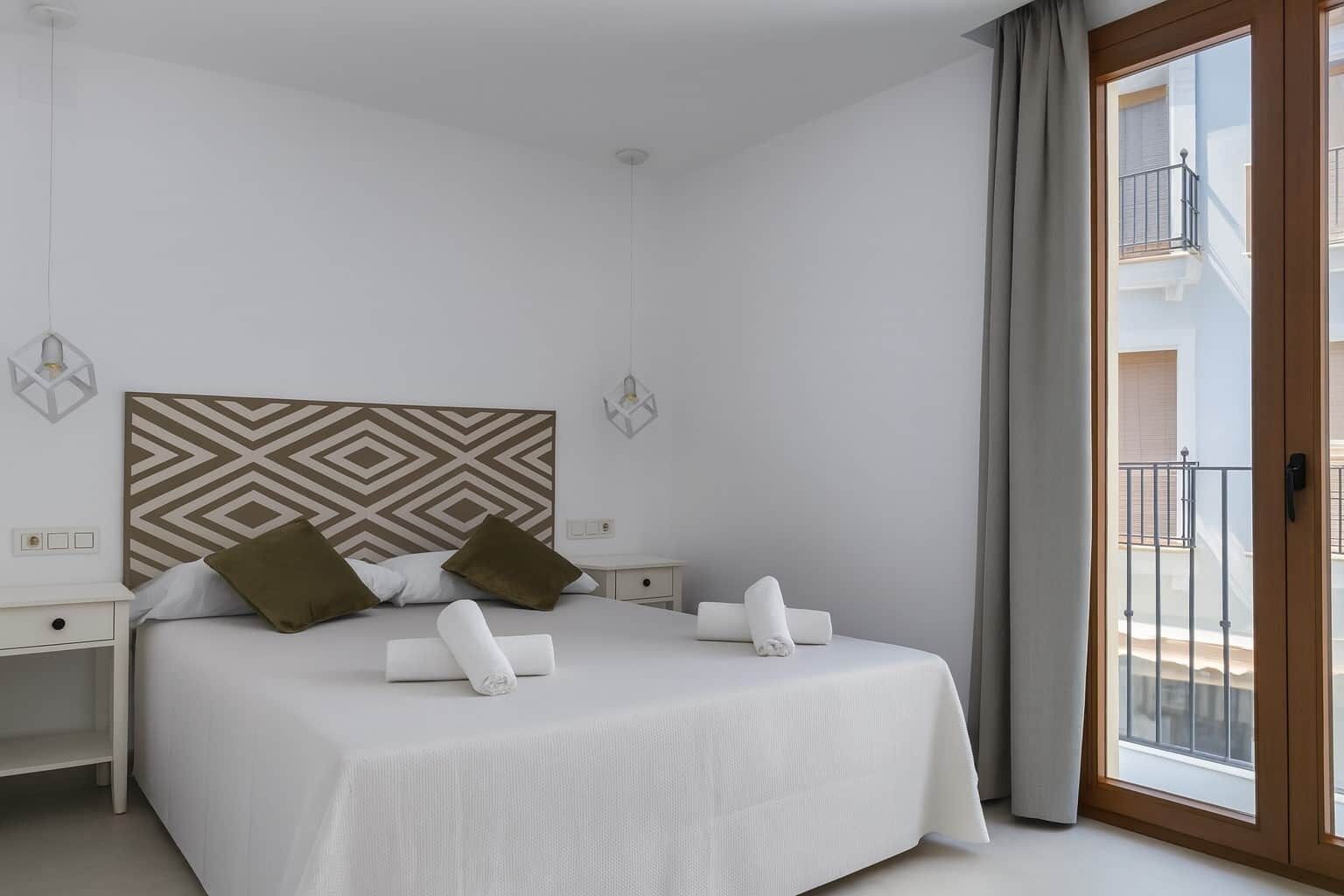 Une chambre d’hôtel moderne dotée d’un grand lit, de deux tables de chevet, d’une tête de lit à motifs géométriques et d’un balcon avec une balustrade.