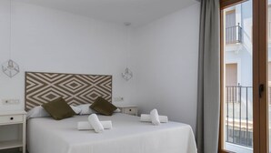 Une chambre d’hôtel moderne dotée d’un grand lit, de deux tables de chevet, d’une tête de lit à motifs géométriques et d’un balcon avec une balustrade.