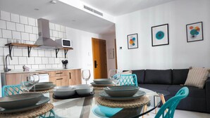Une cuisine moderne avec des carreaux blancs, un four à micro-ondes encastré et une hotte de cuisine en acier inoxydable. On y trouve également un coin repas avec une table en verre et des chaises turquoise.