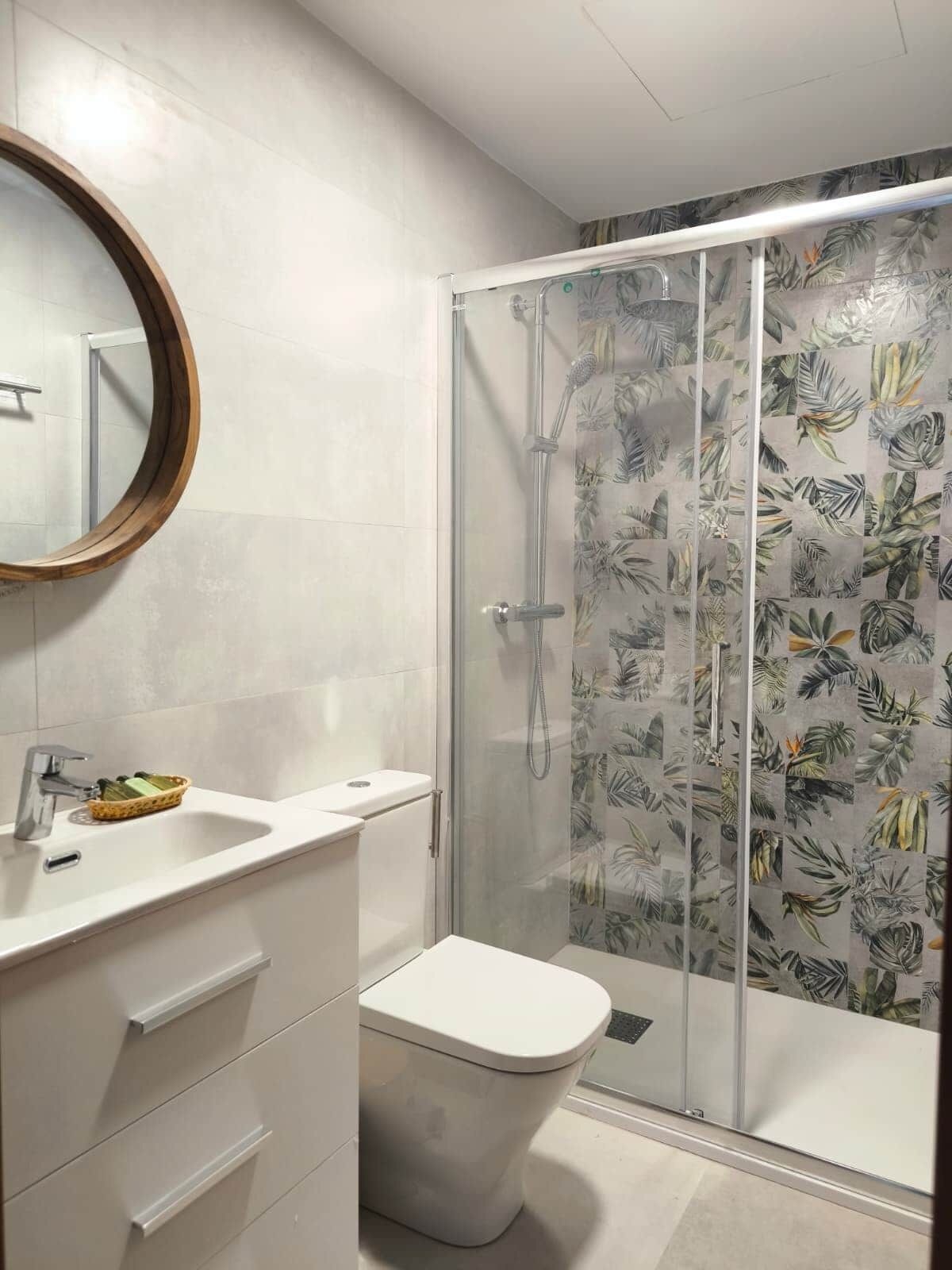 A modern bathroom with a glass shower enclosure, a white toilet, and a vanity with a mirror and sink.