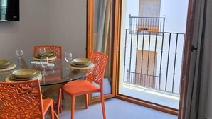 Un coin repas avec une table en verre, des chaises orange et un téléviseur fixé au mur.