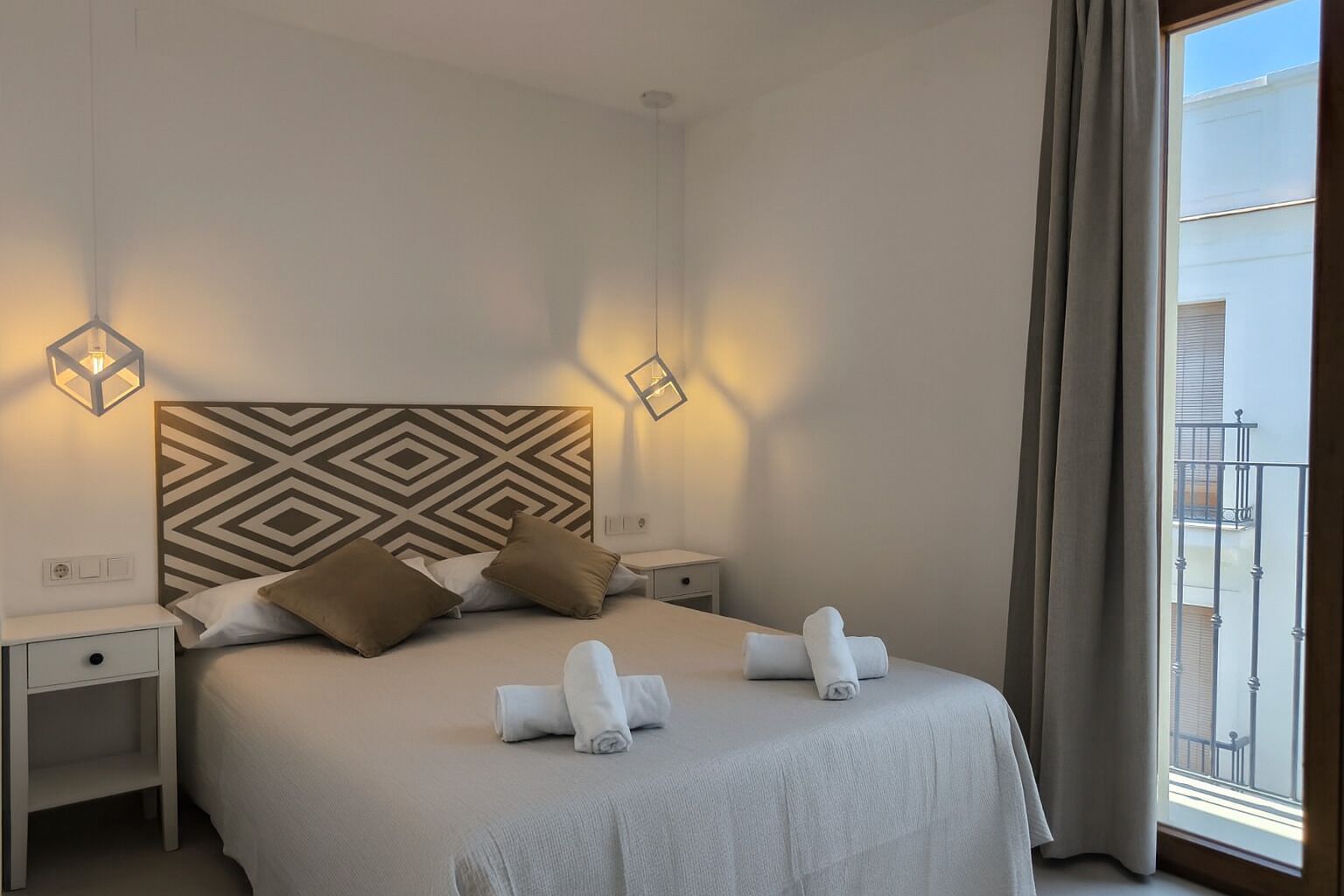 Camera d'albergo con un letto grande, due comodini, una testiera a motivi geometrici e vista su un balcone.