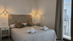 Une chambre d’hôtel avec un grand lit, deux tables de chevet, une tête de lit à motifs géométriques et une vue sur un balcon.