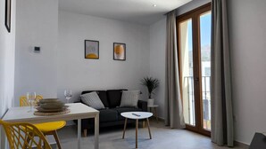 A modern living room with a dining area, a black sofa, yellow chairs, and a large window with curtains. - Pepa · Serenity Apartment (Nerja)