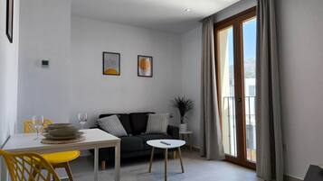 Una sala de estar moderna con comedor, un sofá negro, sillas amarillas y un ventanal con cortinas.