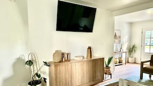 Un salon avec un meuble en bois, un téléviseur à écran plat fixé au mur, une table basse avec un plateau et une plante en pot.