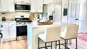 Une cuisine moderne avec des meubles blancs, des appareils en acier inoxydable et un îlot central doté de deux tabourets de bar.