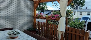 Eine Ziegelwand, ein Holzzaun, ein Tisch mit einem Blumentopf und hängende Blumen.
