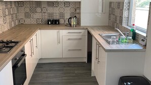 A compact kitchen with white cabinets, a wooden countertop, a stainless steel kettle, and a window with a view of greenery. - Manchester Dream House by Cambrian Street (Manchester)