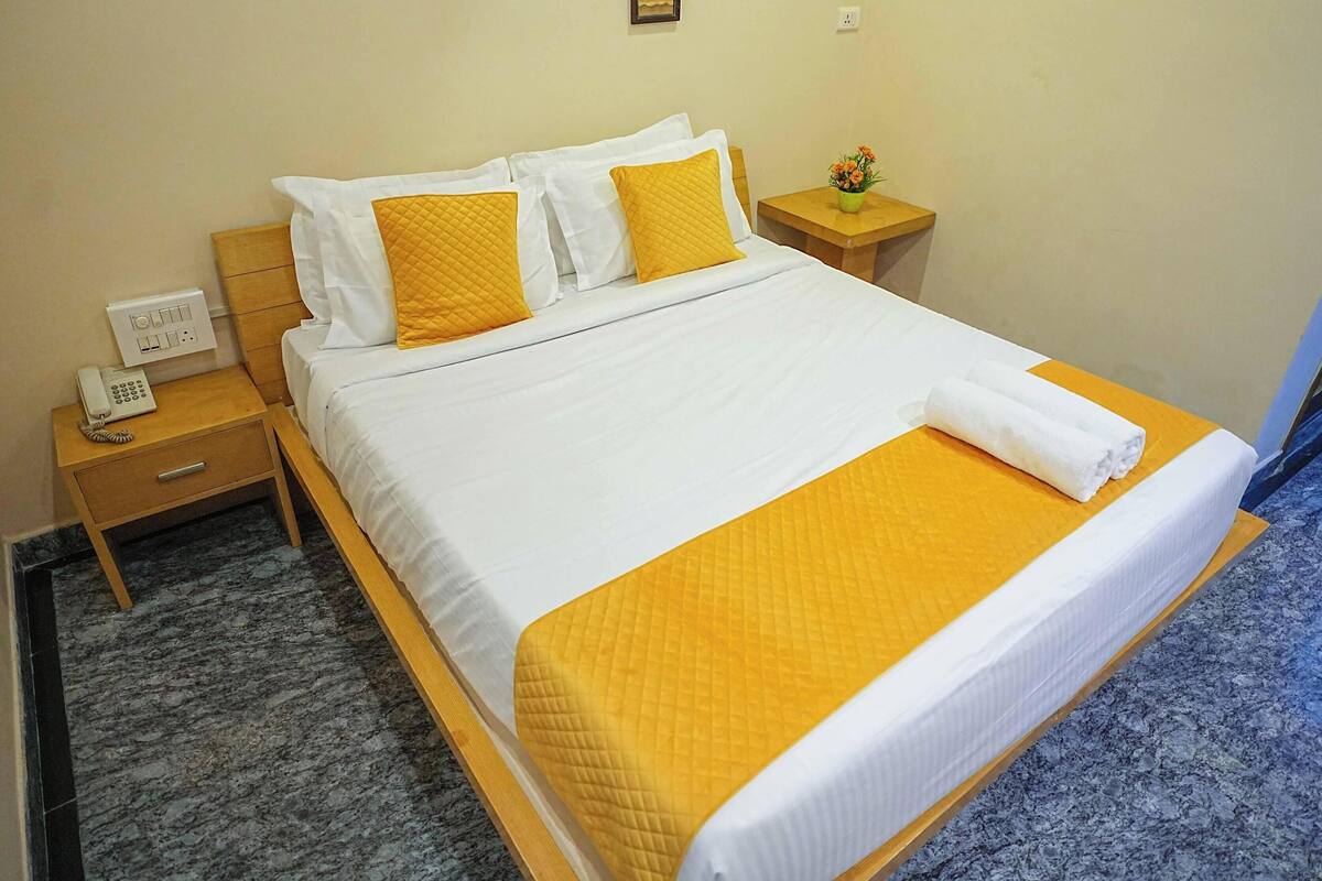 Een hotelkamer met een bed, nachtkastje met telefoon, een bijzettafeltje en een kleintje tafeltje met bloevas.