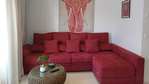 A living room with a red sofa, a round coffee table with a plant, and a tapestry of an elephant on the wall. - BENCOMO SUNSET YOUR FAMILY APARTMENT NEXT TO LORO PARK (Puerto de la Cruz)