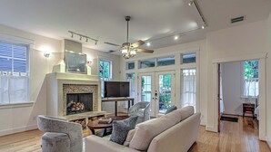 A spacious living room with a fireplace, a ceiling fan, and a large window. - 3BR Retreat near South 1st St. | Walk to SoCo (Austin)