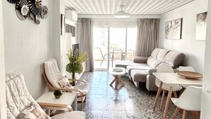 Un ampio soggiorno con soffitto alto, una zona salotto con divani e poltrone, un tavolino da caffè e vista all'esterno attraverso una porta vetrata.