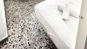 Una camera d'albergo con un letto, un comodino, una finestra con tende e un'opera d'arte appesa al muro.