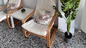Una stanza con due sedie di legno, un tavolino, una pianta in vaso e un elemento decorativo a parete.