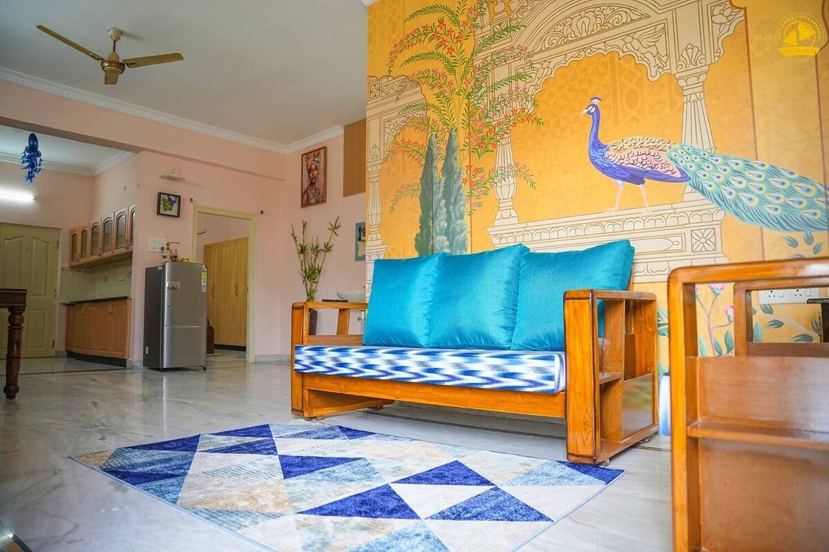 A living room with a sofa, a patterned rug, and a peacock mural on the wall.