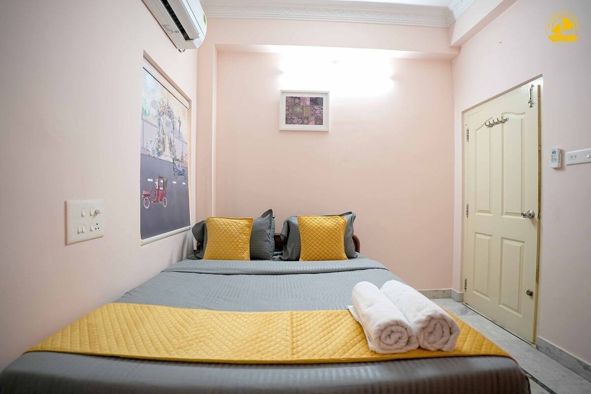 A hotel room with a bed, pillows, a framed picture, an air conditioning unit, and a door.
