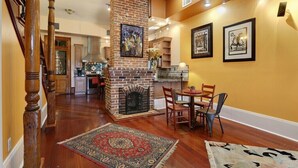 A spacious living area with a brick fireplace, wooden flooring, and a dining table with chairs.