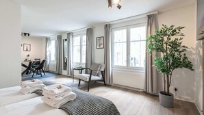 Een hotelkamer met een bed, een bureau, een stoel, een potplant en grote ramen.